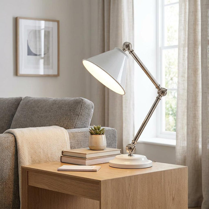 White and polished nickel task lamp with a conical shade on a wooden side table next to a sofa.