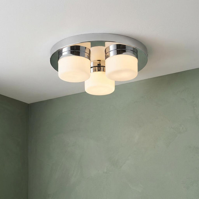 Modern chrome flush ceiling light with three opal duplex glass shades mounted against a green wall.