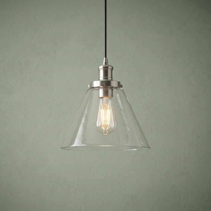 Pyramid-shaped clear glass pendant light with a silver fixture and illuminated Edison bulb against a green wall.