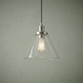 Pyramid-shaped clear glass pendant light with a silver fixture and illuminated Edison bulb against a green wall.