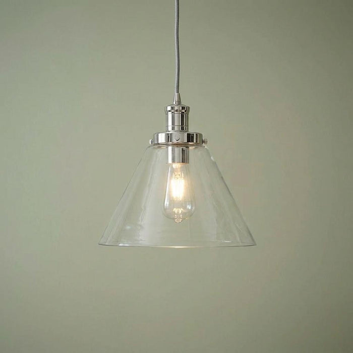 Pyramid clear glass pendant light with chrome hardware and an illuminated bulb against a sage green wall.