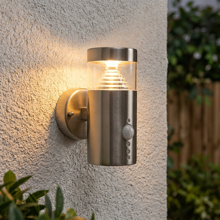 Modern brushed steel Pyramid LED outdoor wall light with a PIR sensor, illuminated on a white textured wall.