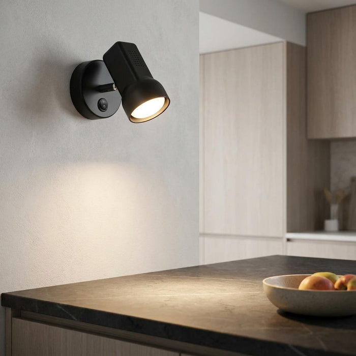 A black adjustable wall spotlight with an integrated switch illuminating a modern kitchen countertop.