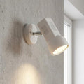 White adjustable single spotlight mounted on a concrete wall, casting light onto a kitchen counter.