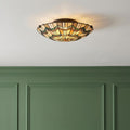Quoizel Alcott Tiffany flush ceiling light with geometric stained glass shade glowing above green paneled walls.