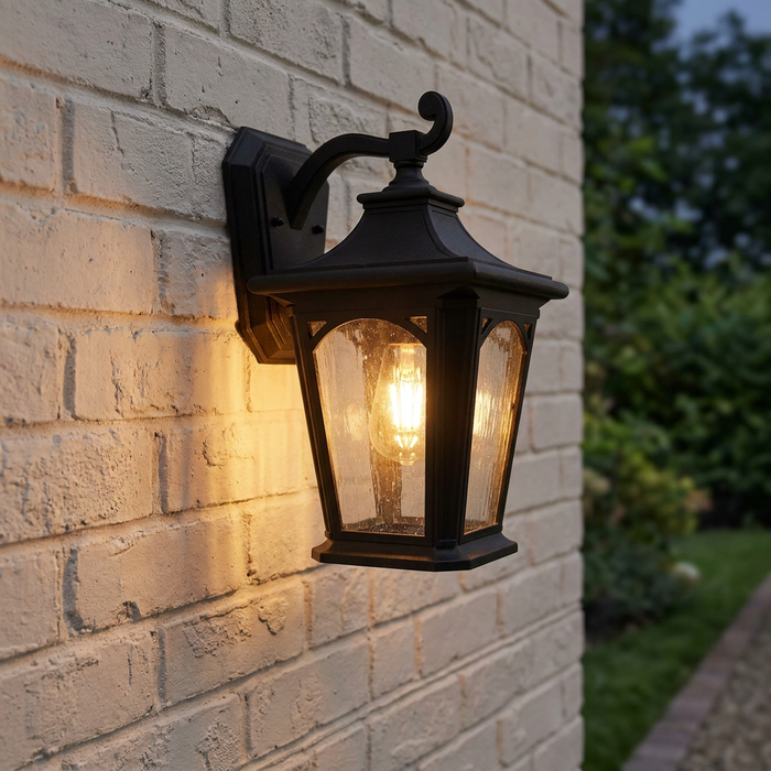 A Quoizel Bedford black outdoor wall lantern with seedy glass lit on a white brick wall at dusk.