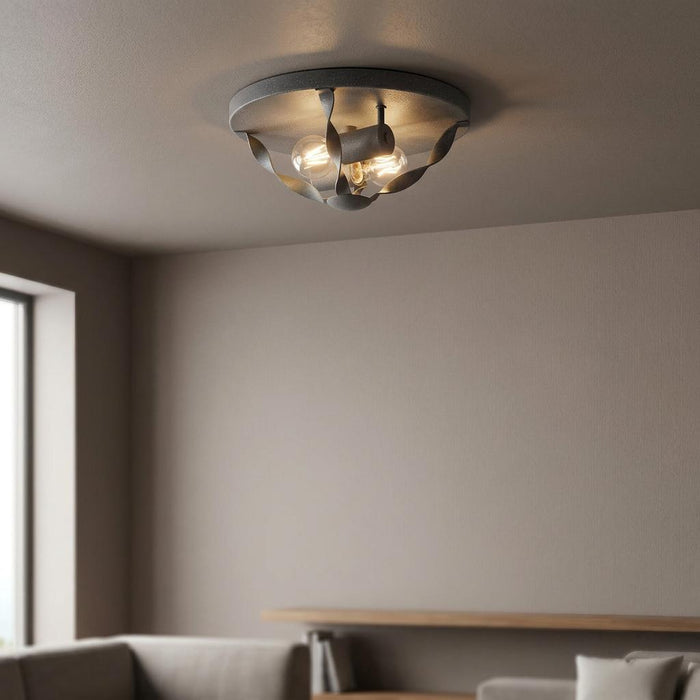 Industrial grey flush mount ceiling light with twisted metal ribbons and glowing bulbs in a neutral living room.