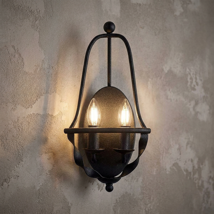 Quoizel Bradbury two-light grey wall sconce with an industrial open frame on a rustic textured wall.