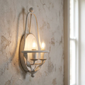 Distressed white two-light wall sconce with candle bulbs mounted on a rustic, weathered plaster wall.