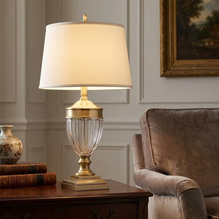 Brass table lamp with a fluted glass base and cream shade illuminated on a wooden side table in a living room.