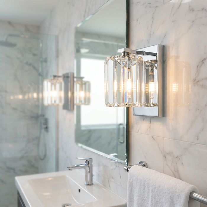 A chrome wall light with a crystal glass shade mounted on a marble bathroom wall next to a mirror.