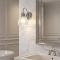 Polished chrome bathroom wall light with a ribbed glass shade mounted on a white marble wall next to a mirror.