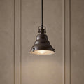 Bronze pendant light with an industrial bell-shaped shade and a glass bottom diffuser hanging in a room.