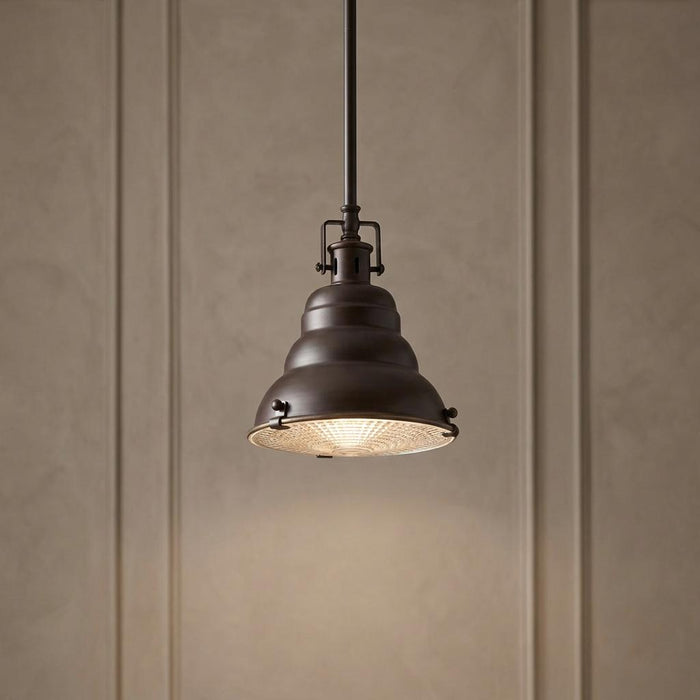 Bronze pendant light with an industrial bell-shaped shade and a glass bottom diffuser hanging in a room.
