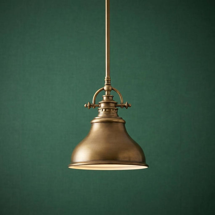 Antique brass mini pendant light with a bell-shaped metal shade against a dark green textured wall.