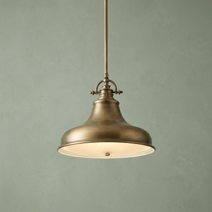 Weathered brass pendant light with a bell-shaped metal shade and diffuser against a green textured wall.
