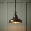A bronze pendant light with a domed shade hangs against a sage green paneled wall, casting a warm glow.