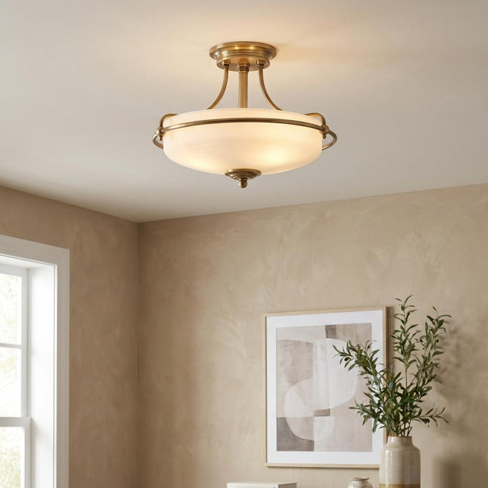 Brass semi-flush ceiling light with a frosted glass bowl shade illuminates a neutral room with beige walls.