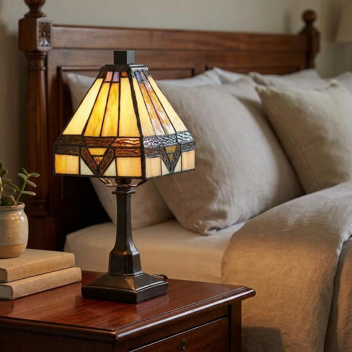 Tiffany-style mini lamp with a geometric stained glass shade on a wooden bedside table in a bedroom.