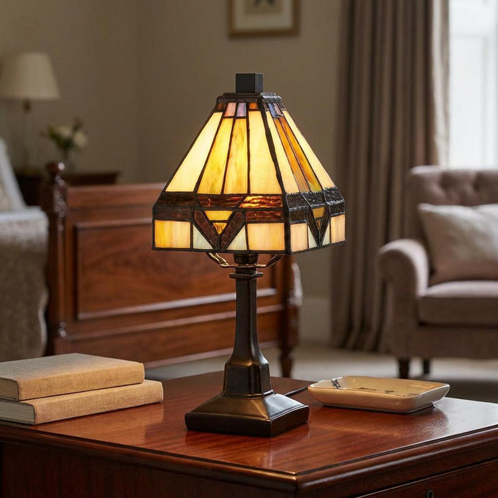 A Quoizel Holmes Tiffany mini lamp with an amber stained glass shade on a wooden bedside table in a bedroom.
