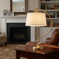 Quoizel Jenkins brass table lamp with cream shade on a wooden side table in a cozy living room.