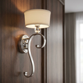 Silver wall light with an elegant S-shaped arm, crystal detail, and cream fabric shade on a dark wood wall.