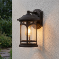 Quoizel Marblehead bronze outdoor wall light with seeded glass and a warm glowing bulb on a white textured wall.