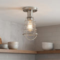 Industrial brushed nickel cage ceiling light with a warm Edison bulb above wooden kitchen shelves.