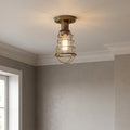 Industrial weathered brass semi-flush mount light with a wire cage and exposed Edison bulb on a white ceiling.