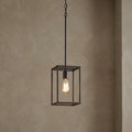 Industrial bronze cage pendant light with an exposed Edison bulb against a textured neutral wall.