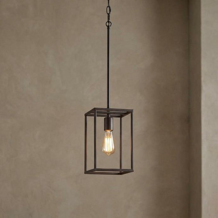 Industrial bronze cage pendant light with an exposed Edison bulb against a textured neutral wall.