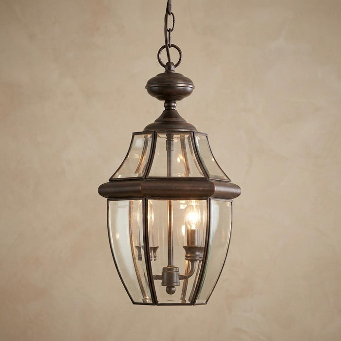 Traditional aged copper outdoor pendant lantern with clear glass panels and three internal candle-style lights.