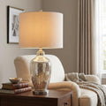 Quoizel Nicolls table lamp with a mercury glass base and beige drum shade on a wooden side table in a living room.