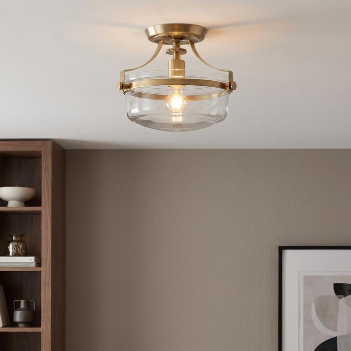 Brushed brass semi-flush ceiling light with a clear glass bowl shade in a contemporary living space.