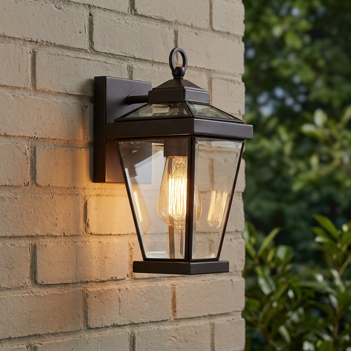 Quoizel Ravine outdoor wall light in western bronze with a glowing Edison bulb mounted on a light brick wall.