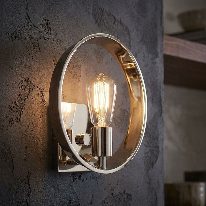 Quoizel Theater Row wall light with a polished silver circular frame and exposed vintage Edison bulb on a textured wall.