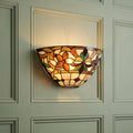 Illuminated Tiffany-style wall light with a floral stained glass shade mounted on a pale green paneled wall.