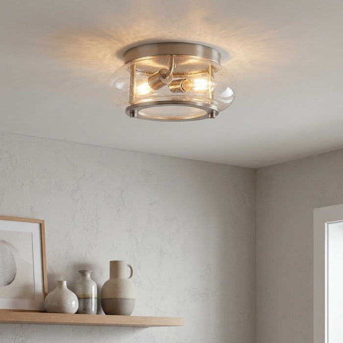Brushed nickel flush mount ceiling light with two bulbs and a seeded glass shade, mounted in a neutral-toned room.