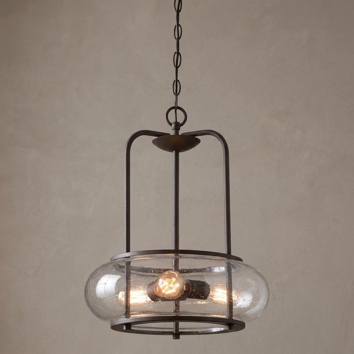 Industrial 3-light pendant with clear seeded glass and dark bronze metal frame on a neutral background.