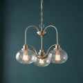 Brushed nickel 3-light chandelier with clear seeded glass globes against a dark teal wall.