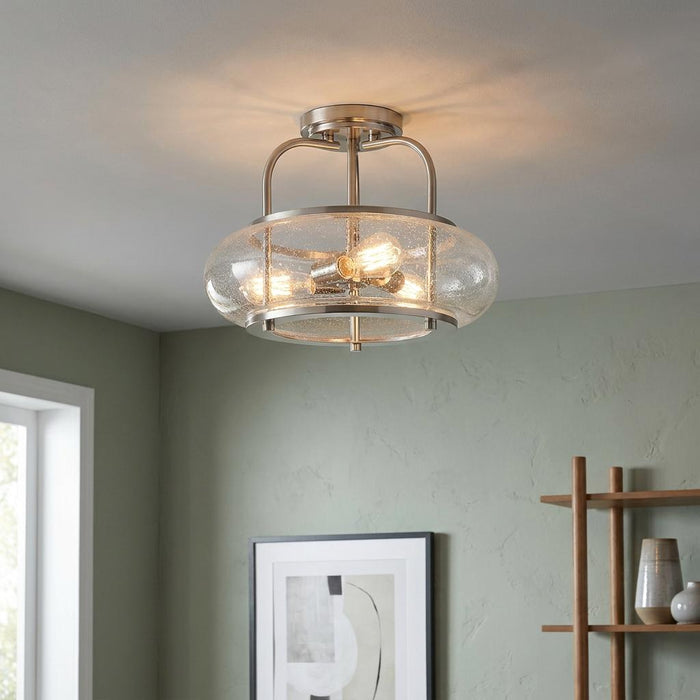 Brushed nickel semi-flush ceiling light with seeded glass shade and three glowing bulbs in a green-walled room.