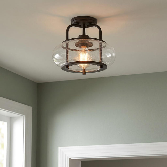 Quoizel Trilogy semi-flush ceiling light with an old bronze frame and seedy glass shade illuminating a room.