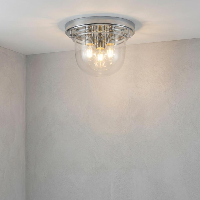 Chrome Quoizel Whistling 3-light bathroom flush mount ceiling light with a clear glass dome on a white ceiling.