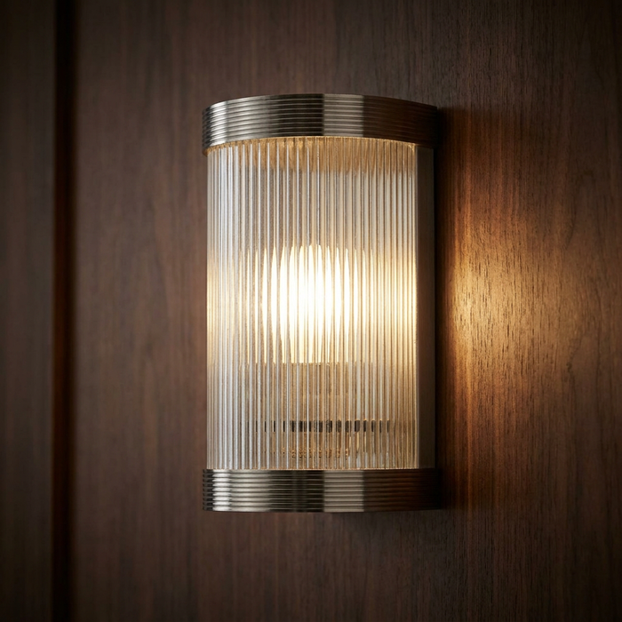 Lit reeded glass and chrome Art Deco wall light mounted on a dark wood panel.