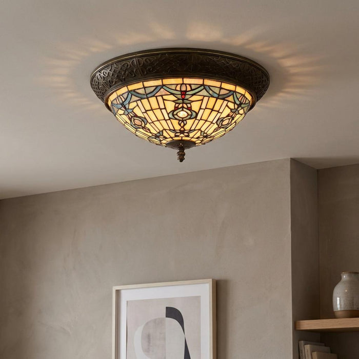 Illuminated Regency flush Tiffany ceiling light with intricate stained glass patterns and a dark bronze ornate frame.