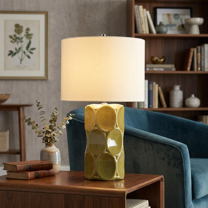 Retro green ceramic table lamp with a textured base and cream shade on a wooden side table in a library setting.