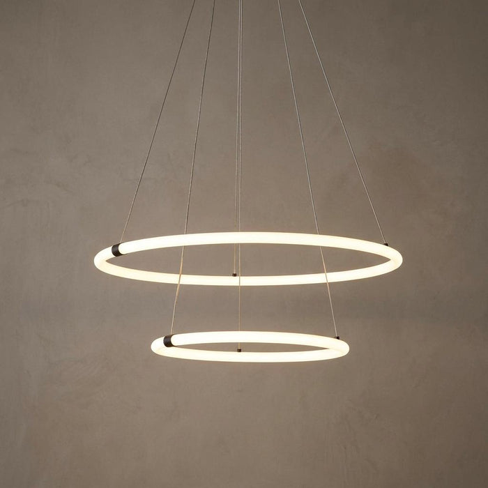 Two tiered glowing opal LED ring pendants suspended by thin cables against a textured neutral wall.