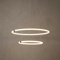 Two tiered glowing opal LED ring pendants suspended by thin cables against a textured neutral wall.
