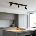 Rez 3 light black modern adjustable plate spot light mounted on a kitchen ceiling illuminating a concrete island.