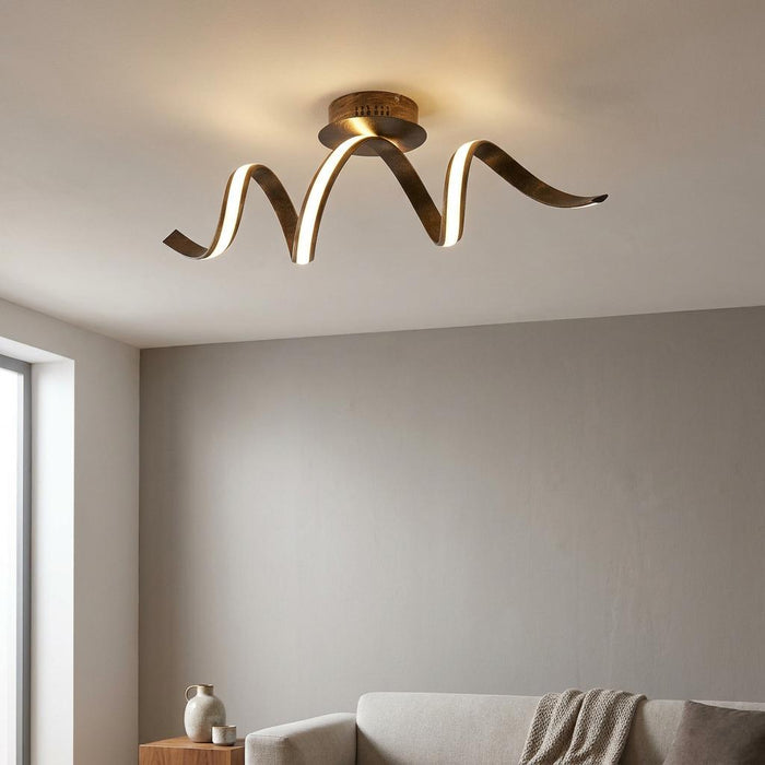 Ribbon LED twist ceiling light with a brown and gold finish glowing above a sofa in a contemporary room.